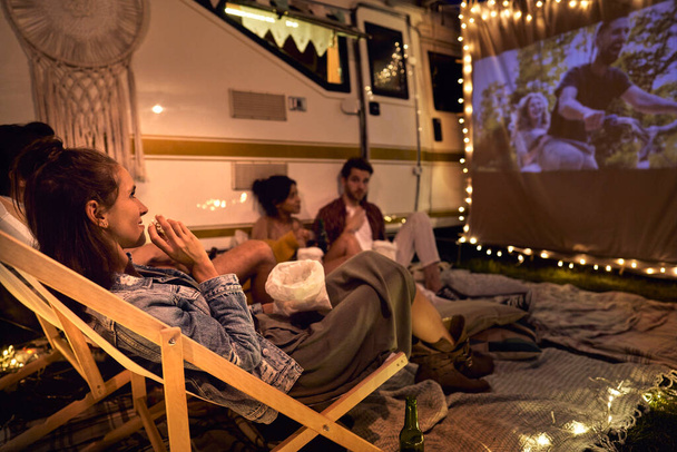 Young cheerful people watching a movie on camping site - Foto, imagen