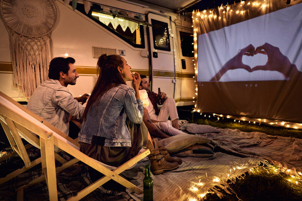 Group of young cheerful people watching a movie on camping site - Foto, imagen