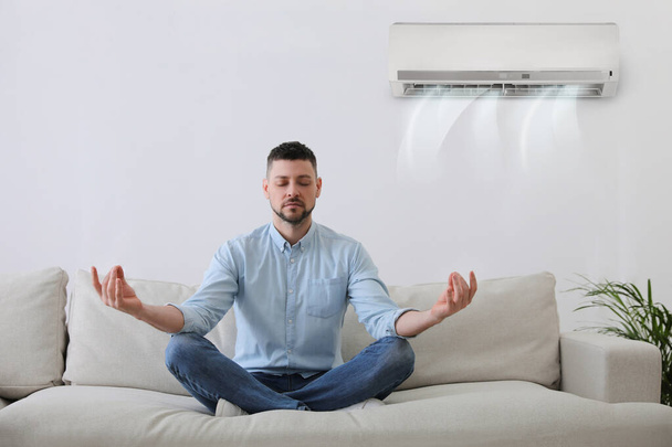 Man resting under air conditioner on white wall at home - Foto, Bild