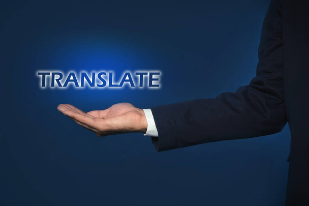 Man showing virtual model of word TRANSLATE against dark blue background, closeup - Fotó, kép