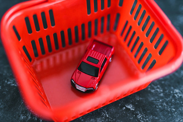 red toy car inside of shopping basket over black marble background, concept of buying a new car - 写真・画像