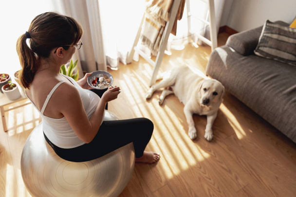 Pregnant woman working at home resting and eating healthy food in the company of her best friend - 写真・画像