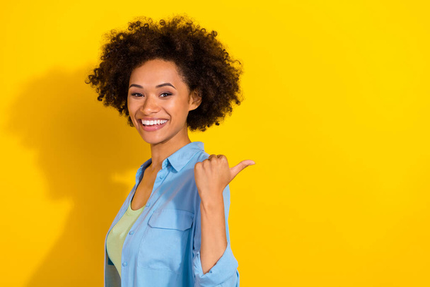 Photo of cheerful promoter cute lady direct thumb finger empty space wear jeans shirt isolated yellow color background - Fotoğraf, Görsel