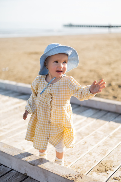 Bébé fille positive en chapeau panama regardant loin sur la jetée à Trévise - Photo, image
