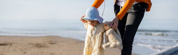 Woman holding toddler kid and toy on beach in Treviso, banner  - Foto, immagini