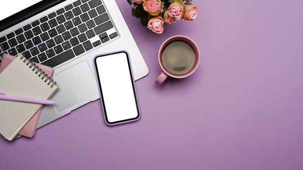 Мобильный телефон с пустым экраном, ноутбук компьютер и чашка кофе на фиолетовом фоне. - Фото, изображение