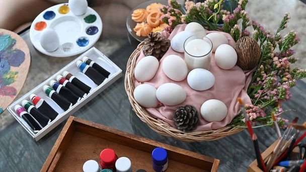 Wiklinowy kosz z jajkami i wiosennymi kwiatami na drewnianym stole. Koncepcja obchodów Wielkanocy. - Zdjęcie, obraz