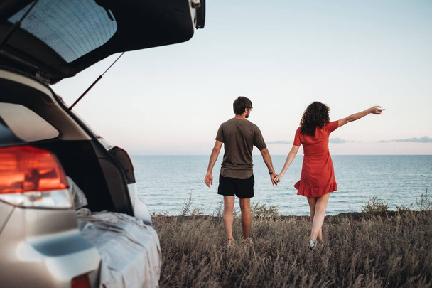 Fiatal pár tartja a kezét Séta a háttér a tenger, a férfi és a nő élvezi a Road Trip on Car - Fotó, kép
