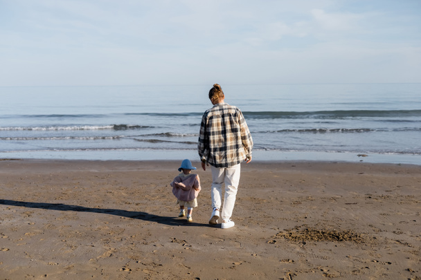 Back view of father and toddler daughter walking on sandy beach near adriatic sea in Italy  - Foto, imagen