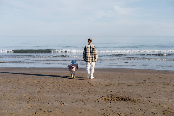 У задньому плані батько з дочкою в панамському капелюсі ходять по пляжу біля моря атріатичного моря в Італії  - Фото, зображення