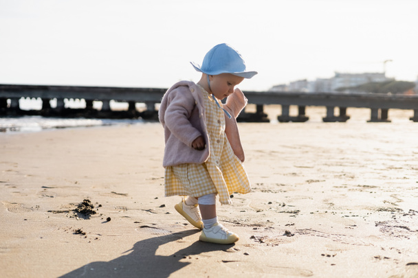 Side view of baby girl in panama hat walking on beach in Italy  - Photo, Image