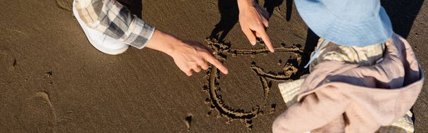 Widok ojca rysującego znak serca na piasku w pobliżu córki, sztandar  - Zdjęcie, obraz