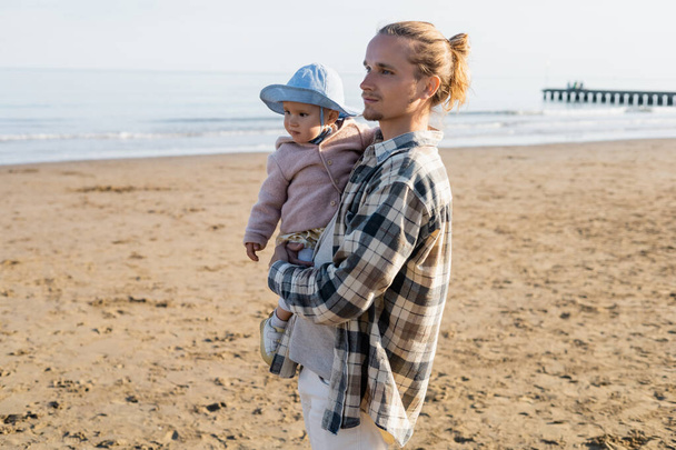 Hombre de pelo largo sosteniendo a su hija bebé en la playa en Italia  - Foto, Imagen