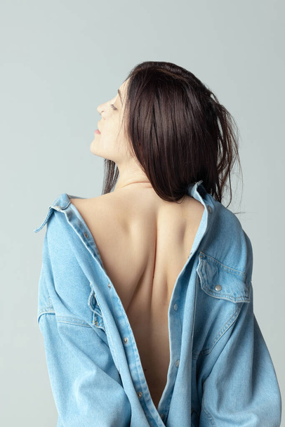 Beautiful shape of female back. One beautiful woman posing in shirt isolated over grey studio background - Foto, Imagen
