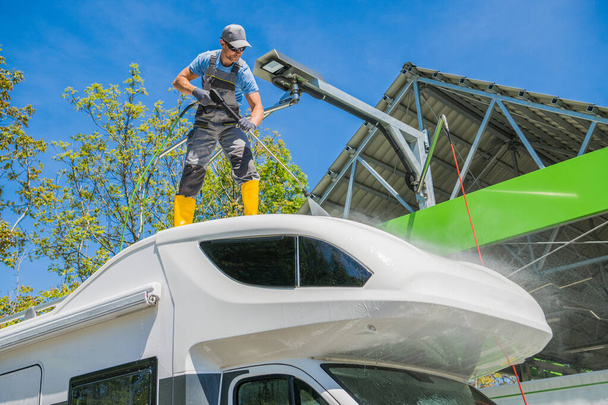 Caucasian RV Camper Rentals Worker Cleaning Motorhome Using Powerful Pressure Washer While Staying on the Vehicle Roof.  - Photo, Image