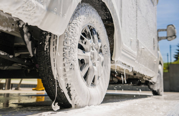 RV Camper Van Covered by Active Washing Foam Close Up Photo. Washing Recreational Vehicle Motorhome in a Car Wash. - Photo, Image