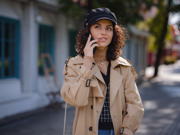 Outdoors lifestyle fashion portrait of pretty young lady talking on smartphone. Young hispanic or Armenian woman wearing elegant style standing at Moscow city. - Foto, Imagen
