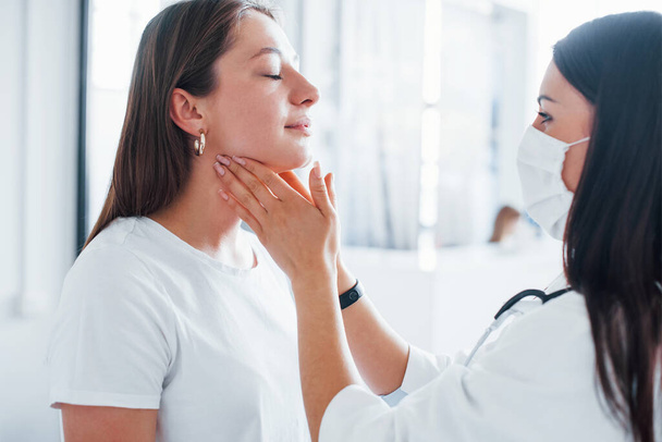 Checking lymph nodes and throat. Young woman have a visit with female doctor in modern clinic. - Foto, immagini