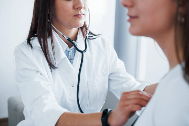 Using stethoscope. Young woman have a visit with female doctor in modern clinic. - 写真・画像