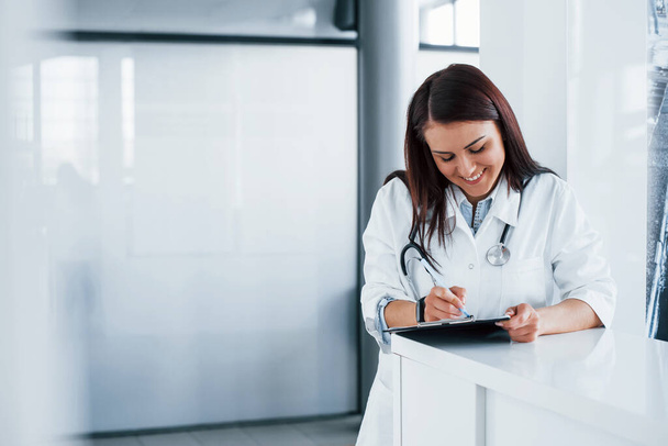 With notepad. Young nurse indoors in modern clinic. Conception of healthcare. - Foto, imagen