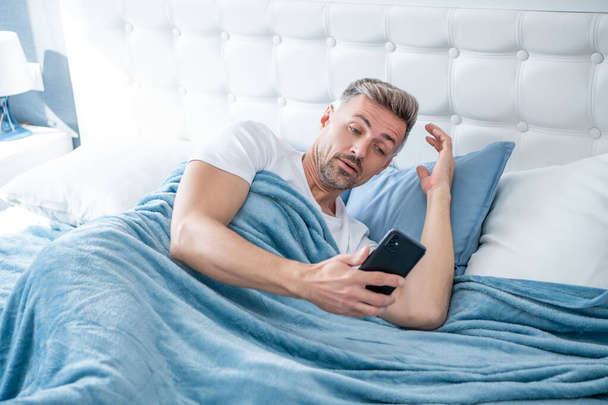 amazed mature man in bed chatting on phone - Photo, Image