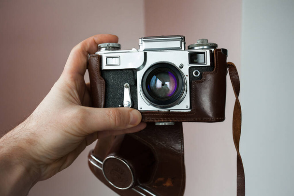 Käsi pitää vanhaa analogista neuvostofilmikameraa ruskeassa nahkalaukussa, kevyellä taustalla, sisätiloissa. - Valokuva, kuva