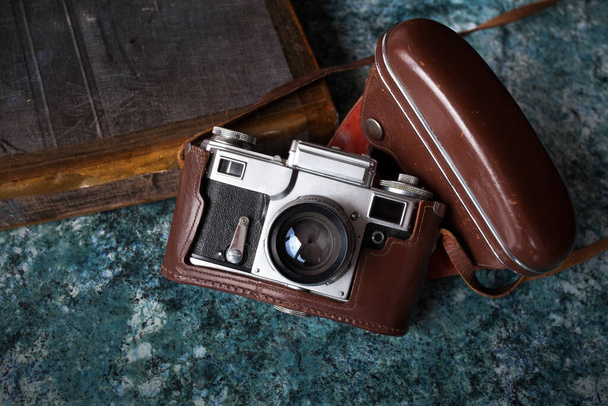 Vintage Neuvostoliiton kamera ruskea nahka tapauksessa sijaitsee kuvioitu sininen pöytälevy. Lähellä on vanha kirja.. - Valokuva, kuva