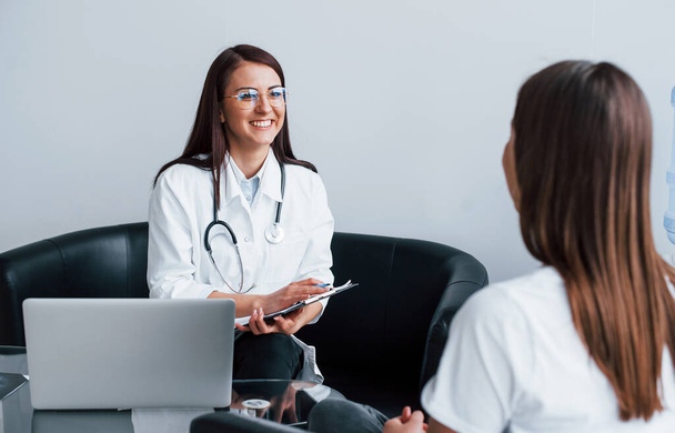 Sitting and talking. Young woman have a visit with female doctor in modern clinic. - Foto, Bild
