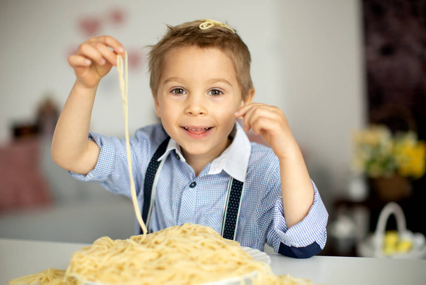 Cute preschool child, blond boy, eating spaghetti at home, making a mess everywhere, funny moments - Foto, Imagen