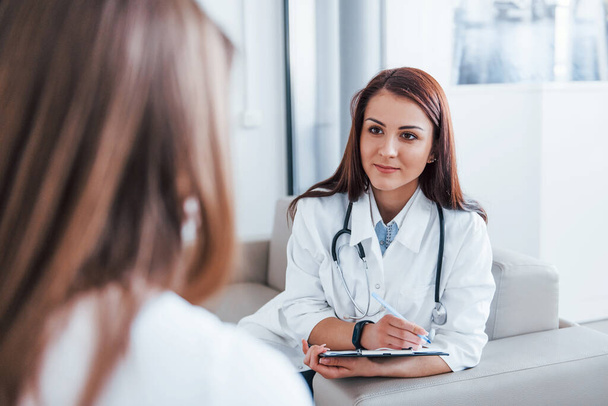 Sitting and talking. Young woman have a visit with female doctor in modern clinic. - 写真・画像