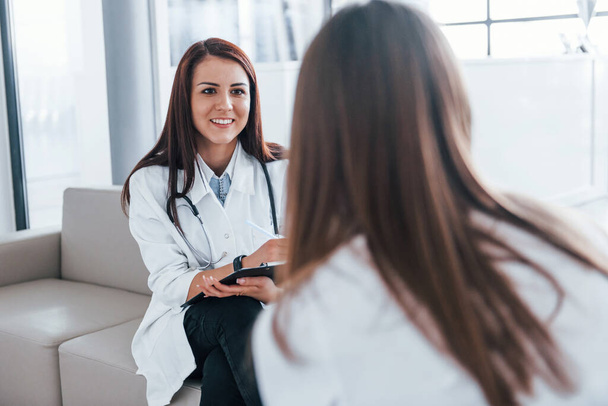 Sitting and talking. Young woman have a visit with female doctor in modern clinic. - Foto, Imagen