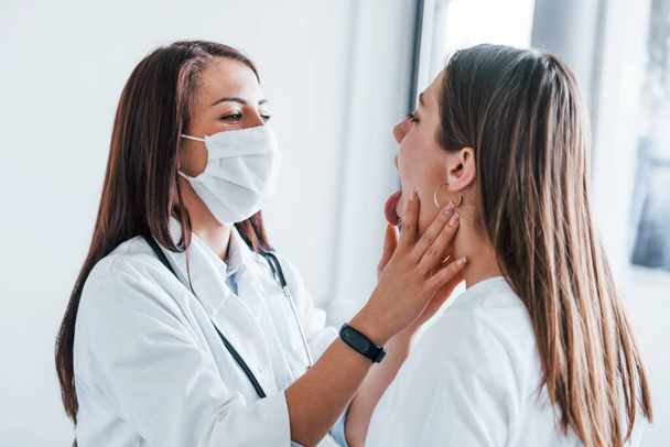 Checking lymph nodes and throat. Young woman have a visit with female doctor in modern clinic. - Photo, image