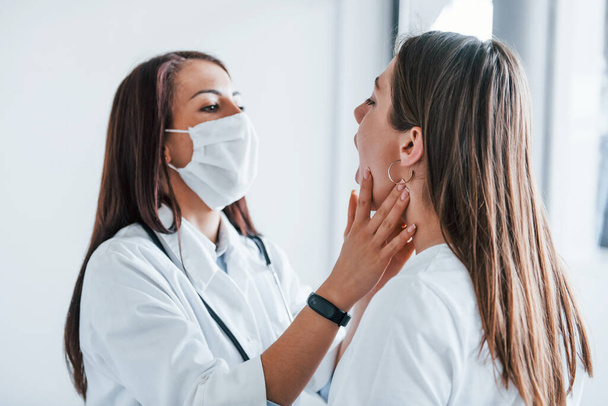 Checking lymph nodes and throat. Young woman have a visit with female doctor in modern clinic. - Foto, Imagem