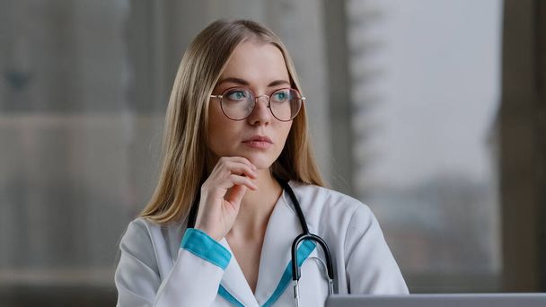 Focused caucasian female pensive nurse smart woman practitioner doctor thinking of problem diagnosis appointment solution makes decision comes up with idea typing laptop online advice to patient - Foto, Bild