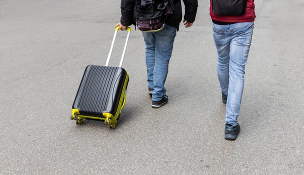 Молодой человек вытаскивает черный чемодан на улицу. Мужчина уходит со своим багажом, ожидая транспортировки. Вид сзади. Копирование пространства - Фото, изображение