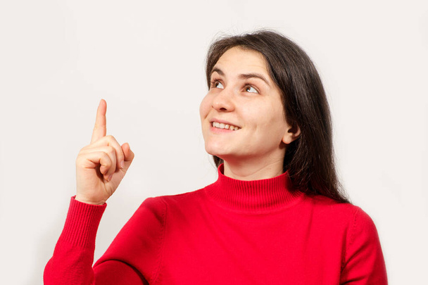 Une femme brune en rouge lève les yeux et pointe son doigt vers un endroit pour le texte - Photo, image