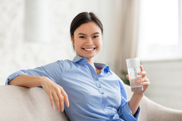 Portrait of cheerful asian woman holding glass of water - 写真・画像