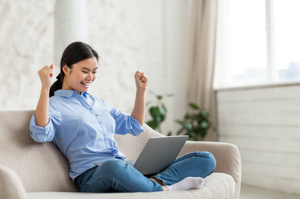 Cute asian lady with laptop celebrating success, home interior - Photo, Image