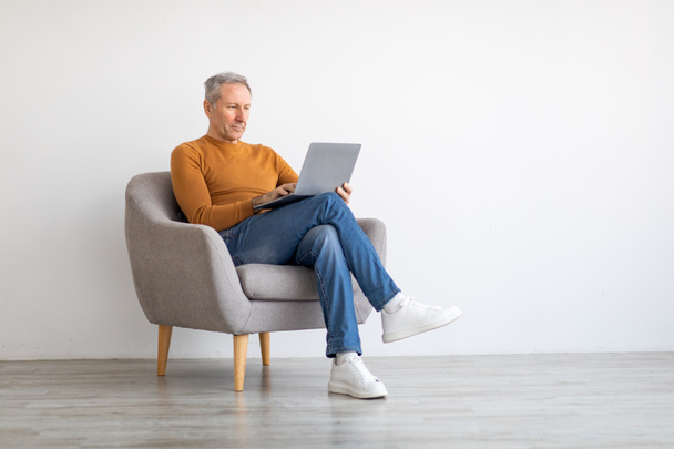 Zelfverzekerde volwassen man met laptop zittend op stoel - Foto, afbeelding