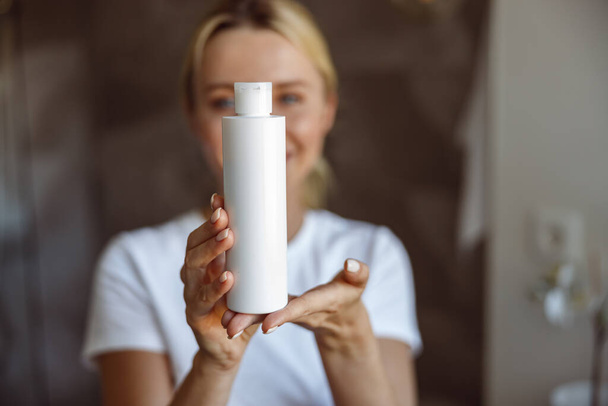 Close up of face lotion or moisturizer in hands of attractive young blonde woman. Beauty care. - 写真・画像