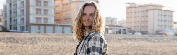 Young long haired man standing on beach in Italy, banner  - Фото, изображение