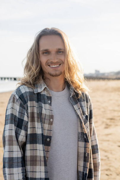 Portrait of smiling long haired man looking at camera on beach in Italy  - Foto, Imagem