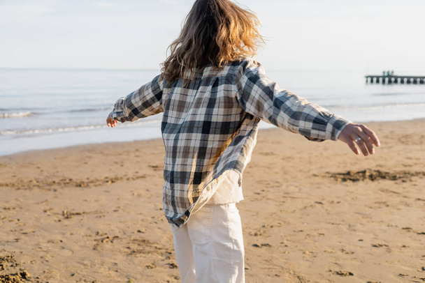 Back view of long haired man in checkered shirt walking on beach in Treviso - Photo, Image
