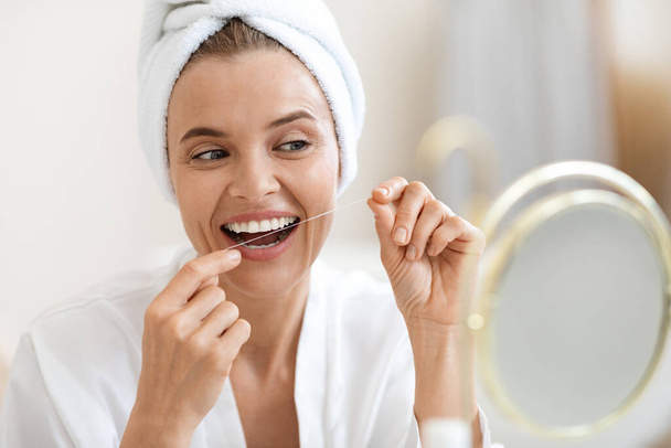 Mujer adulta usando hilo dental, limpiando sus hermosos dientes blancos - Foto, Imagen