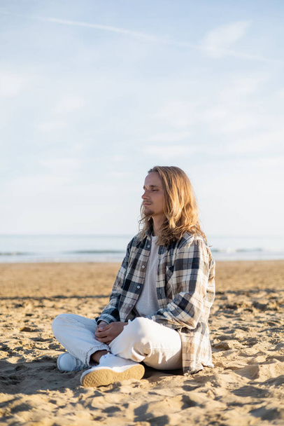 Long haired man meditating on beach in Italy  - Photo, Image