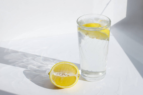 a glass of water with lemon on a white sunny background - Fotoğraf, Görsel