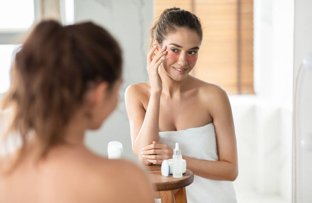 Female Applying Under Eye Patches Moisturizing Skin Standing In Bathroom - Photo, image