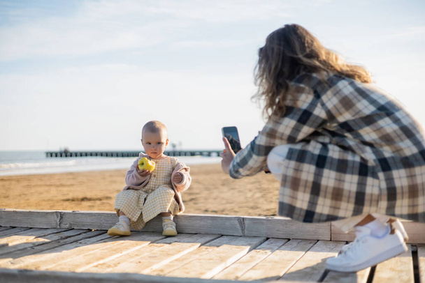 Blurred man taking photo of baby girl with apple on pier in Italy  - Fotoğraf, Görsel