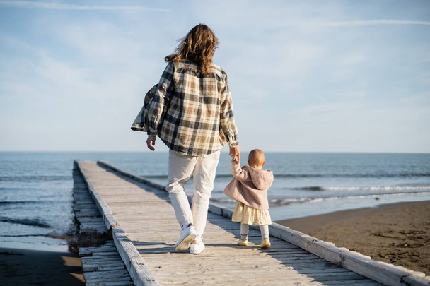 Back view of long haired man and toddler girl walking on wooden pier near adriatic sea in Italy  - Valokuva, kuva