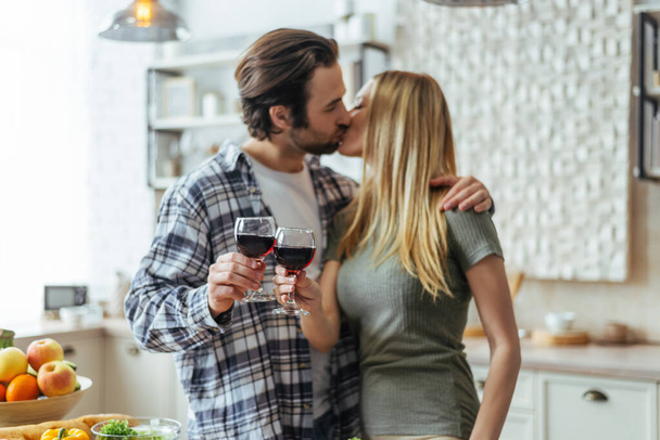Happy handsome caucasian millennial man with stubble kisses woman blond, cheers with glasses - 写真・画像